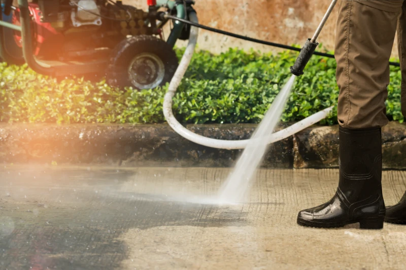 Worker cleaning driveway with gasoline high pressure washer splashing the dirt.